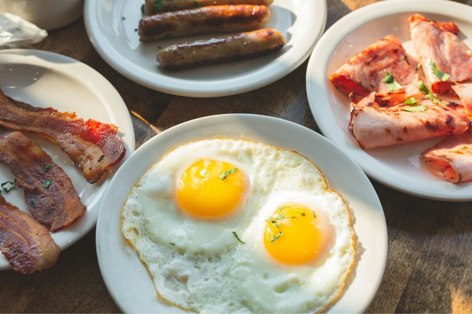 Plates of eggs, bacon, sausage, and ham.