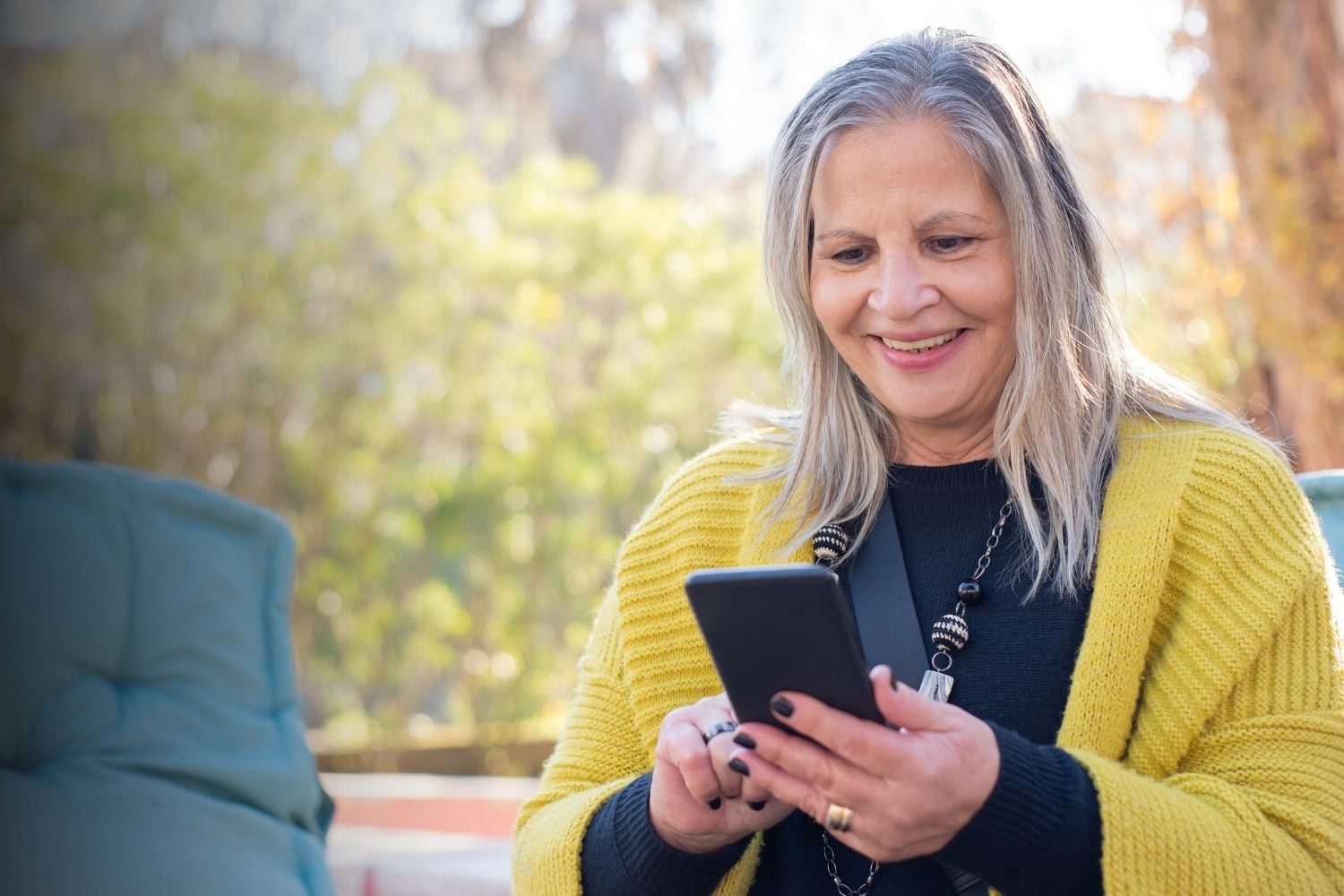 A woman wearing a sweater looks at her phone and smiles. 