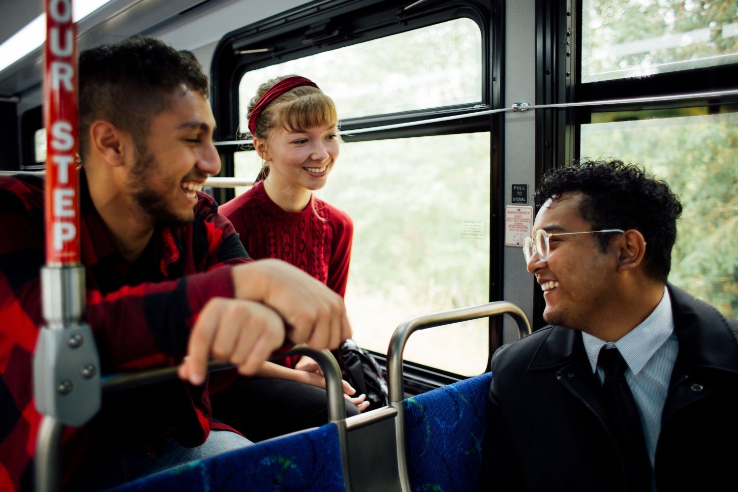 Three young people are smiling and talking as they ride the bus together.