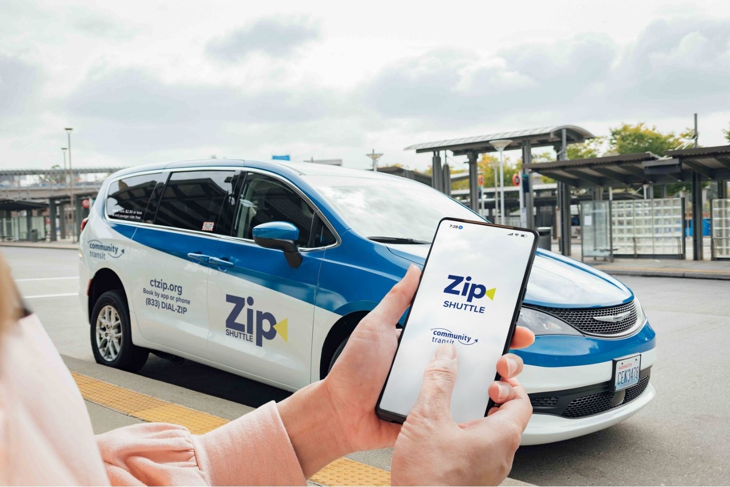 A woman holds a mobile phone with the Zip Shuttle app on screen.