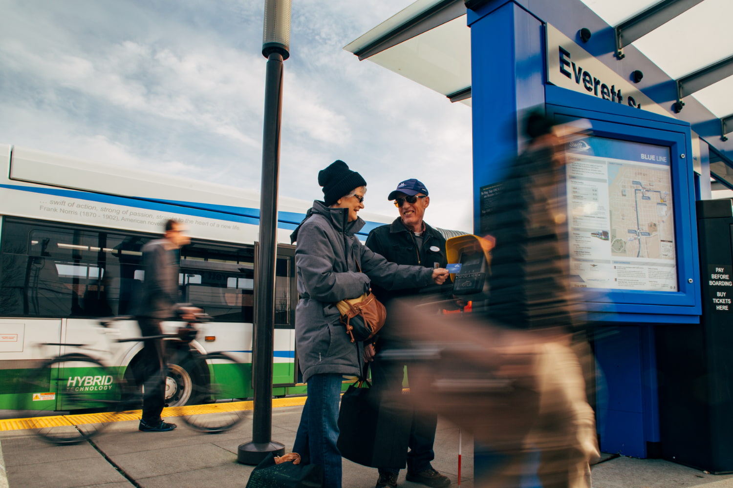 A smiling older couple tap their ORCA card at the Everett Swift Station