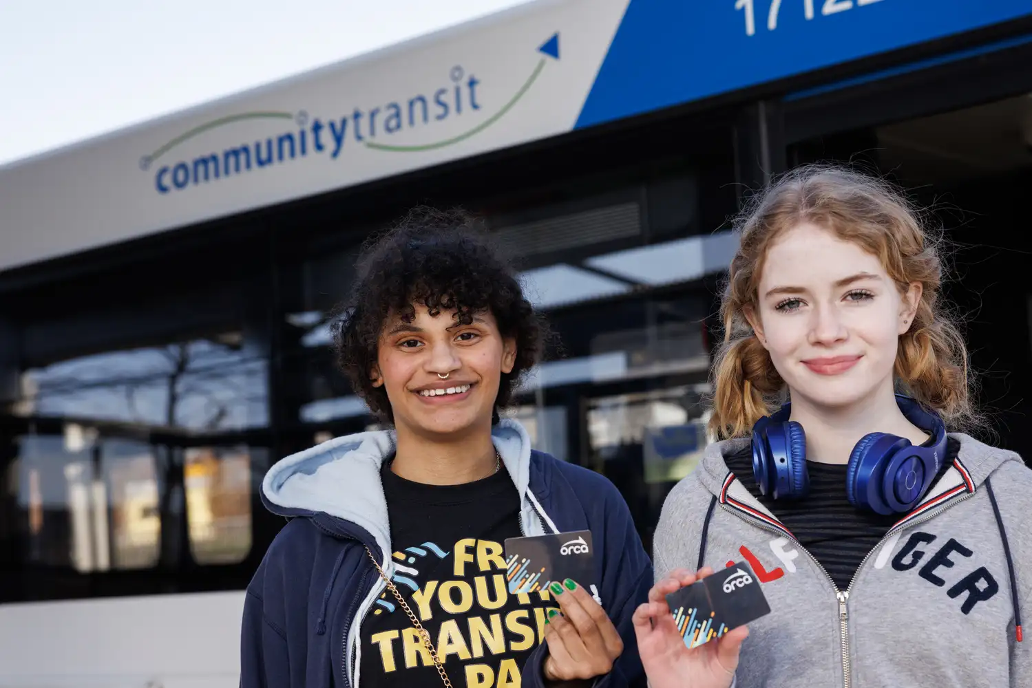 two youth riders pose with their free ORCA passes in front of a CT bus