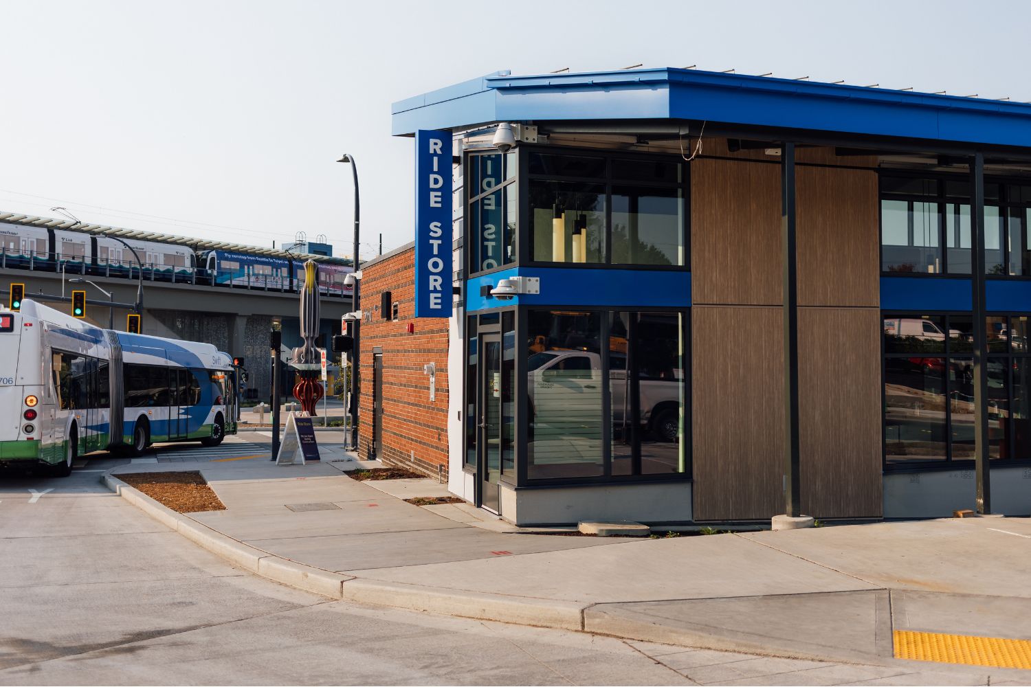 A picture of the outside of the Community Transit Ride Store. A brown building with a blue roof, and a sign that says "Ride Store." A bus is driving by the building.