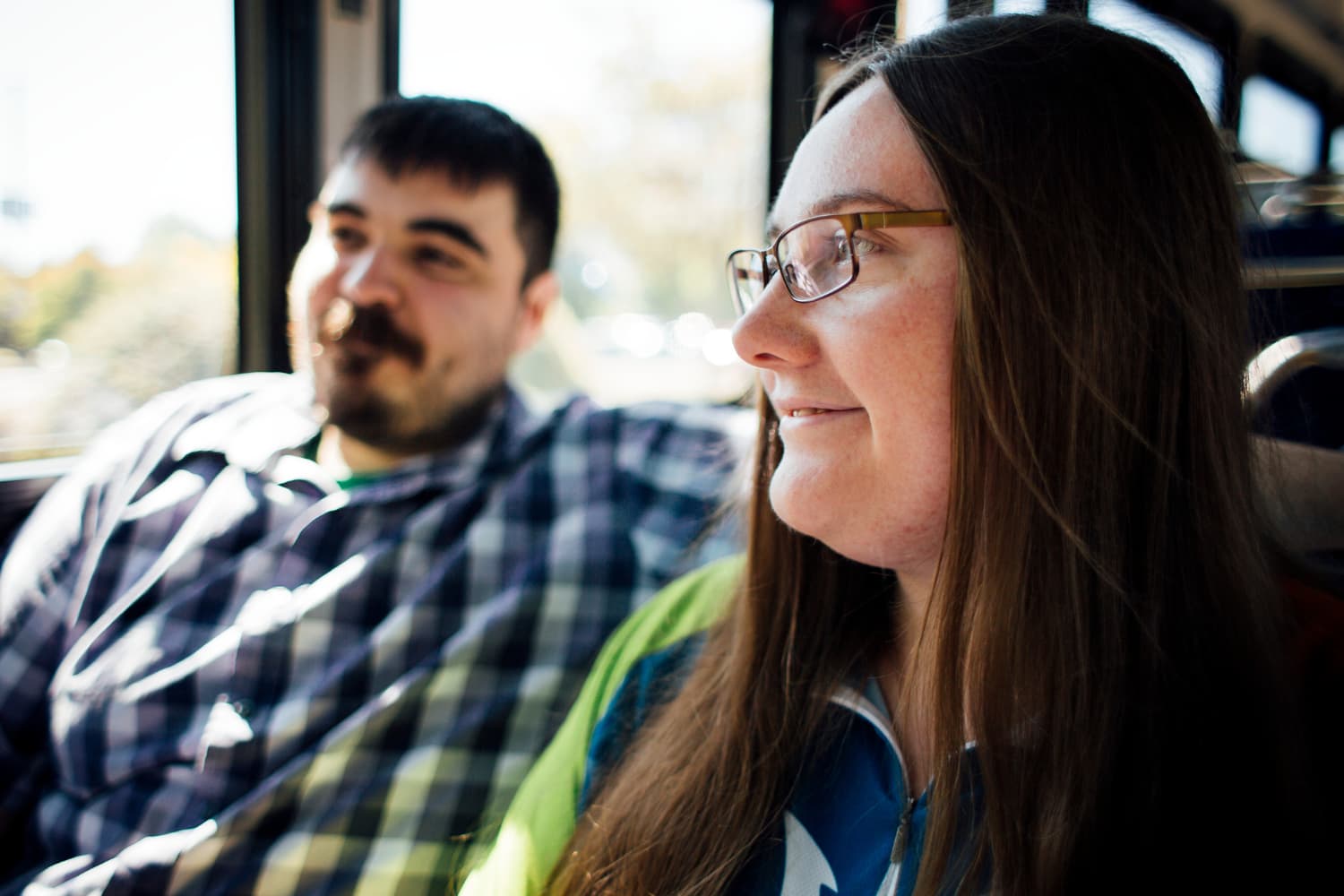 A man and a woman sit side by side on the bus, looking out the window.