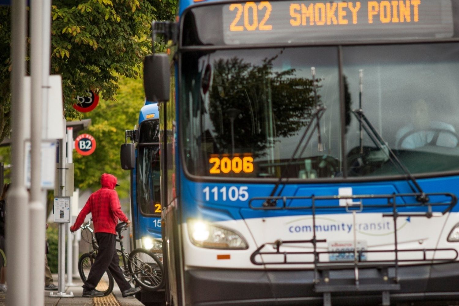 A person unloading their bike off of a bus. A bus with a headway sign for Route 202 is in the foreground.