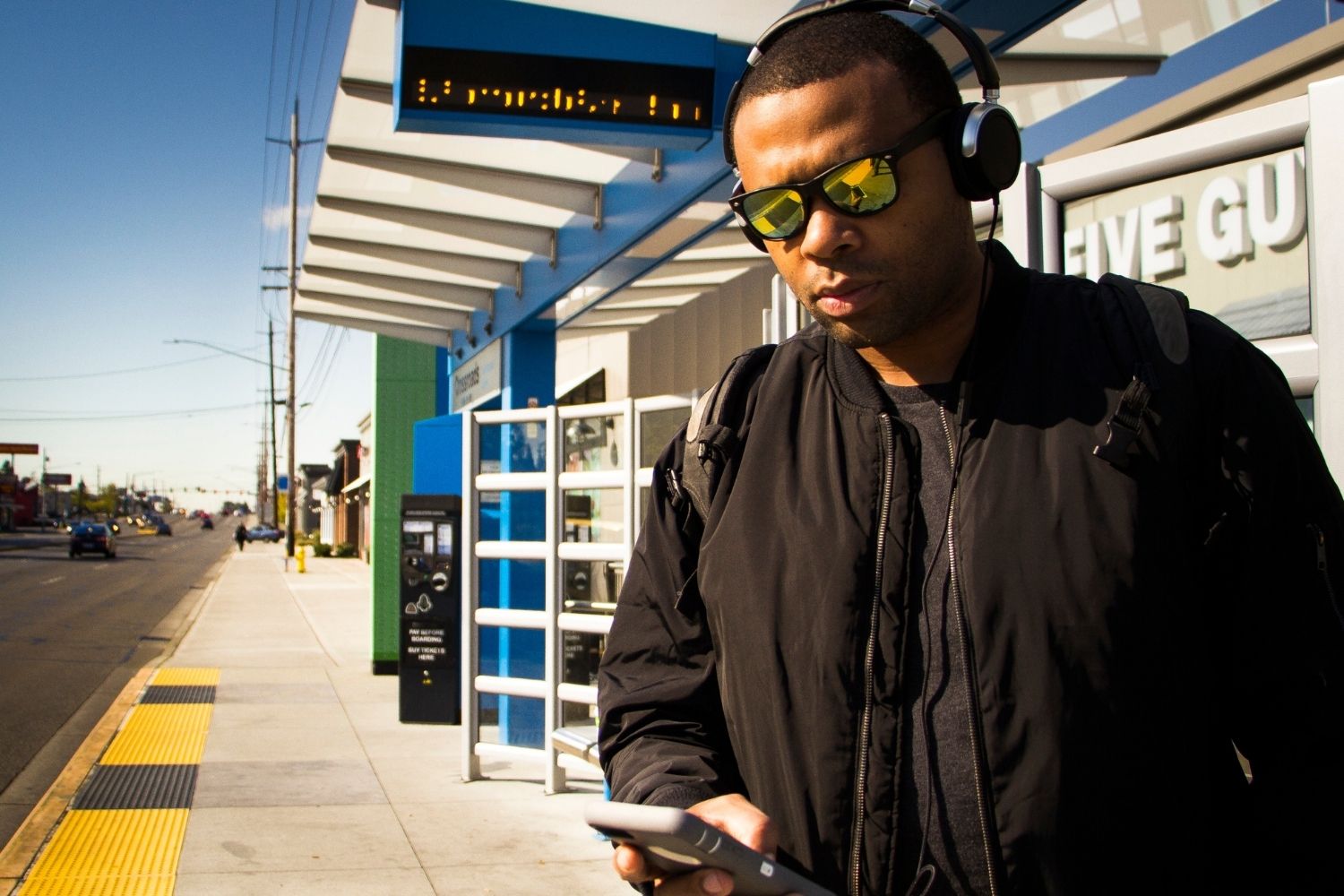 A man wearing sunglasses checks his phone at a bus stop.