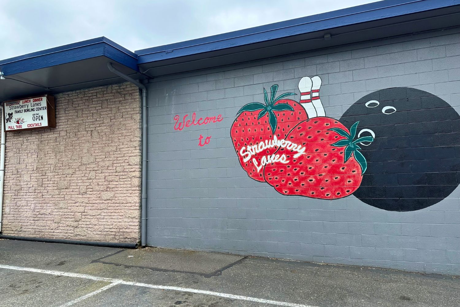 The outside of Strawberry Lanes in Marysville. A grey building with a mural of a red strawberry and a black bowling ball painted on it. 