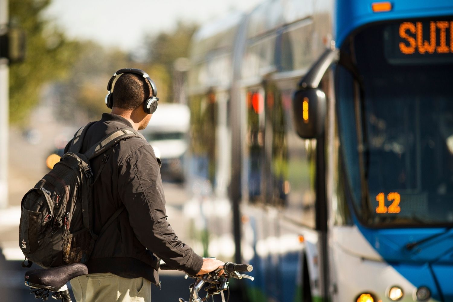 A person wearing headphones waiting to board a Swift bus. The person has a bike.