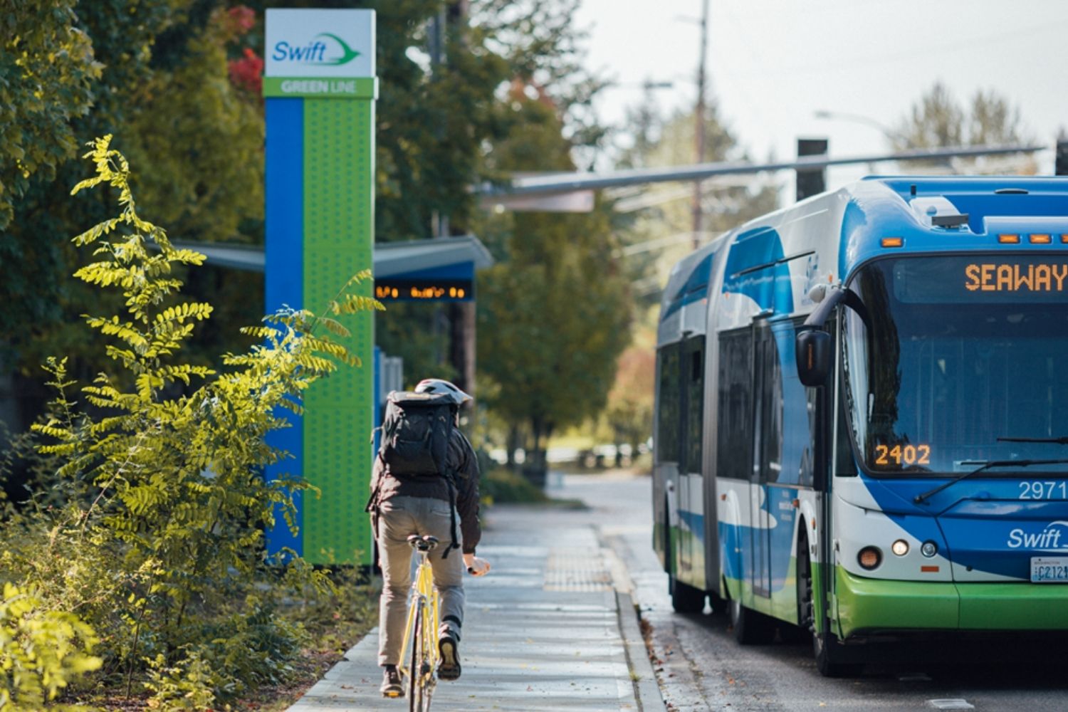 A man riding a bike towards a Swift Green Line Station. 