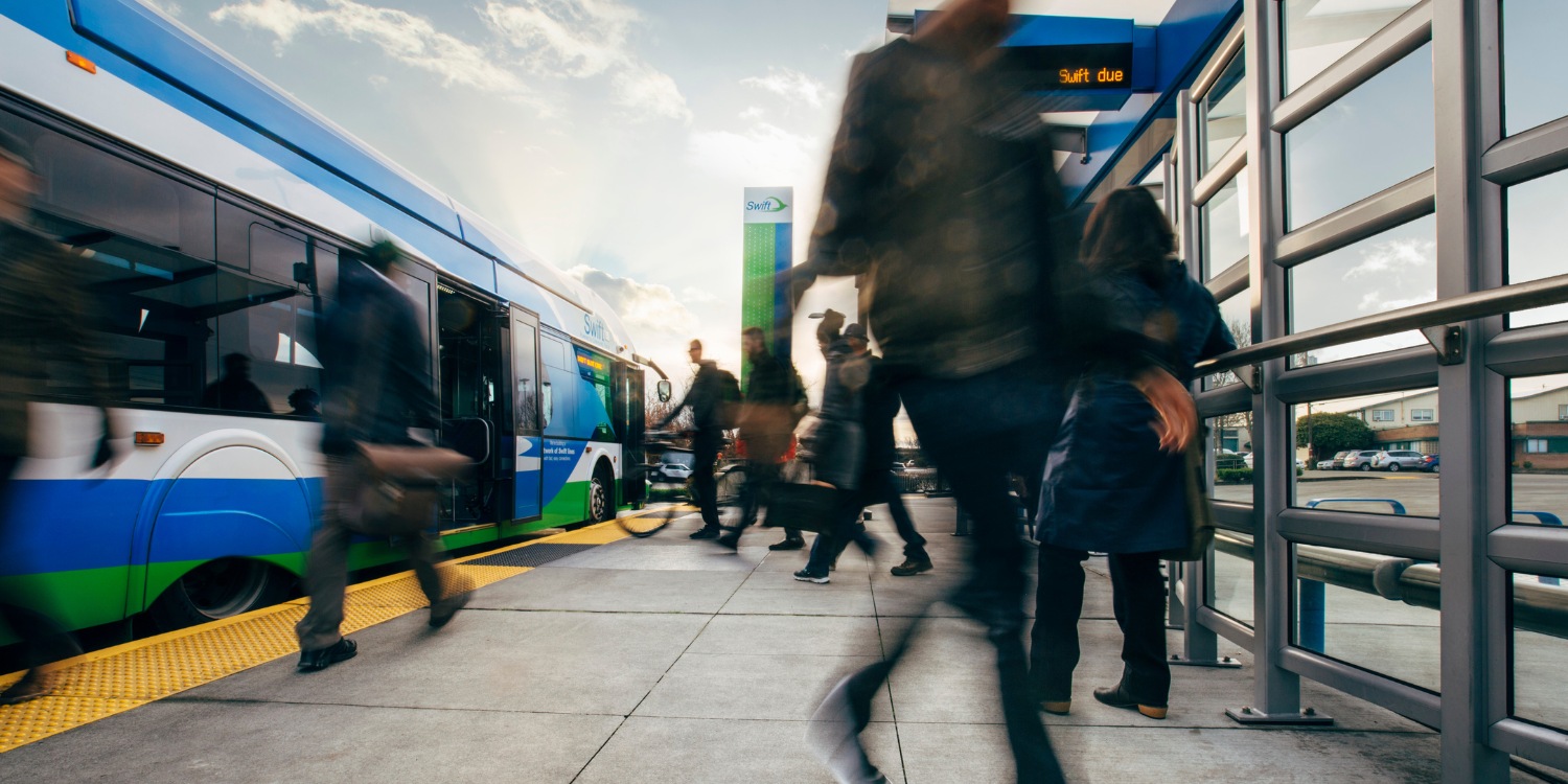 Commuters hurry to board a Swift bus at a transit station during a busy time.