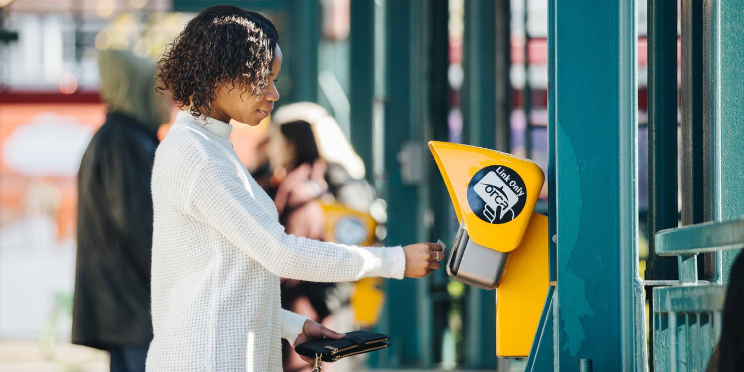 A young woman taps her payment card at an ORCA reader at a light rail station