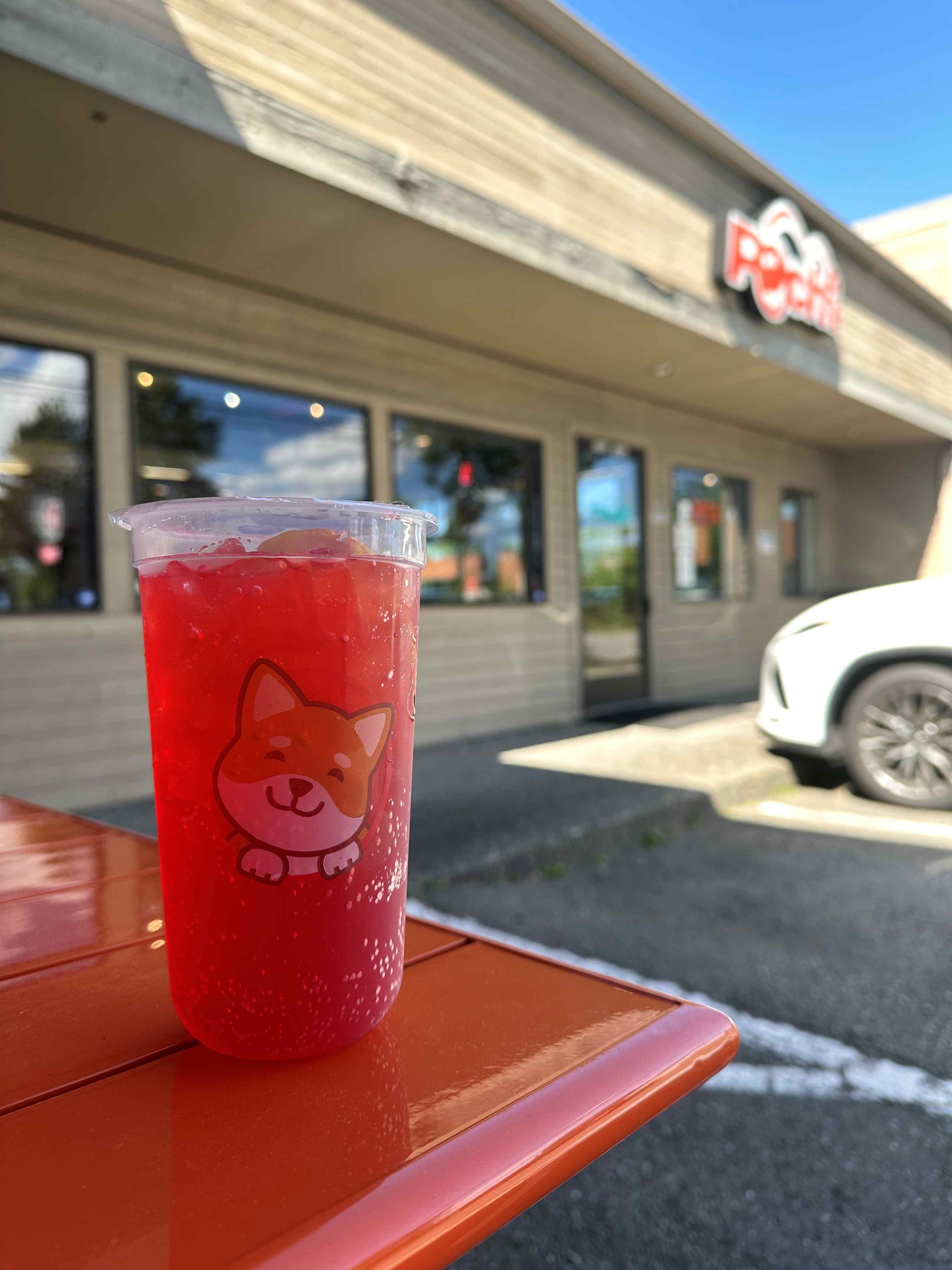 An iced tea beverage from Pochi in the foreground with the store and logo behind it