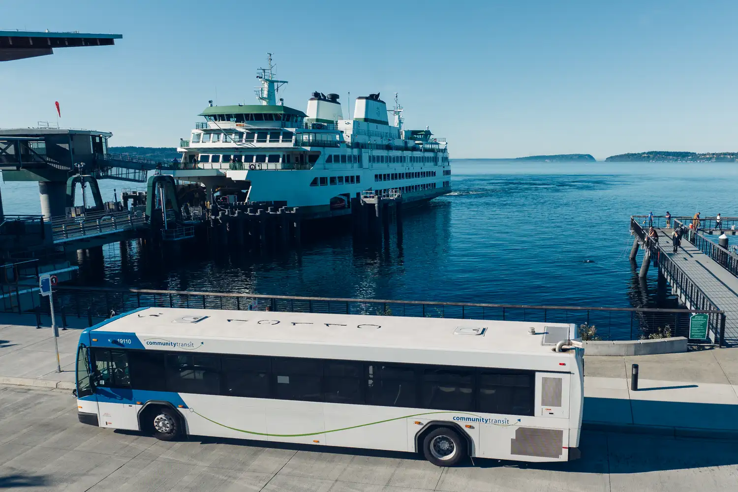 a Community Transit bus parked at the Mukilteo ferry terminal with a ferry docking in the background