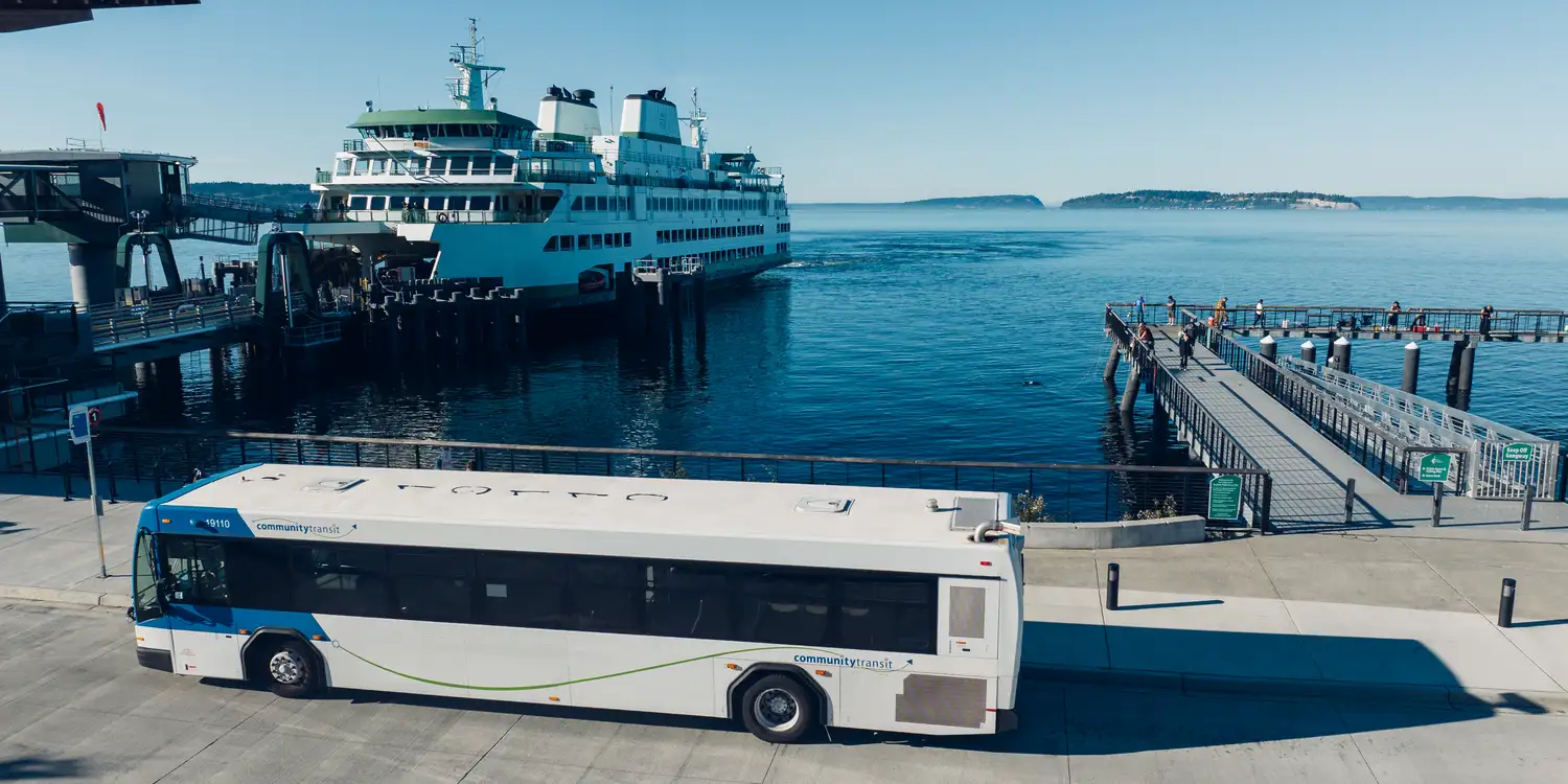 a Community Transit bus parked at the Mukilteo ferry terminal with a ferry docking in the background