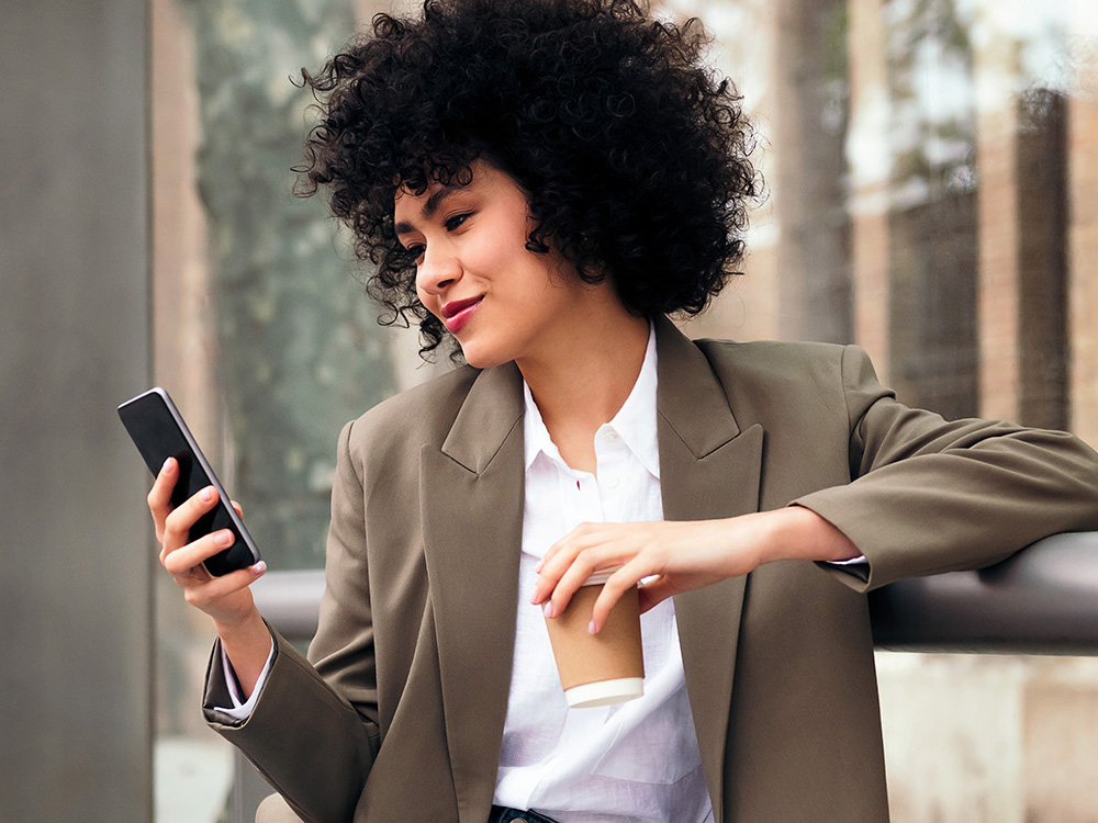 A woman gets Rider Alerts on her phone while waiting at a bus stop.