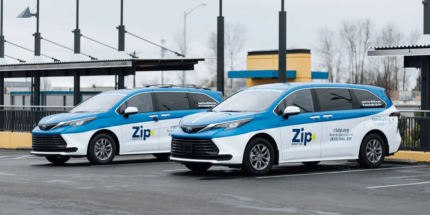 Two Zip Shuttle vans parked at a transit center