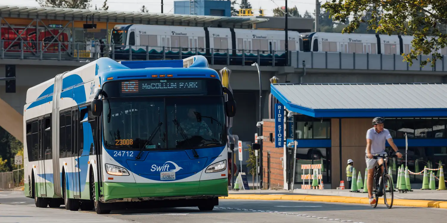 a Swift bus arriving at Lynnwood City Center Station with the CT Ride Store and Link light rail in the background